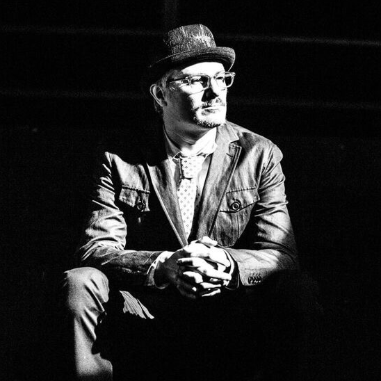 Jim wearing a hat and sitting in a theatrical space